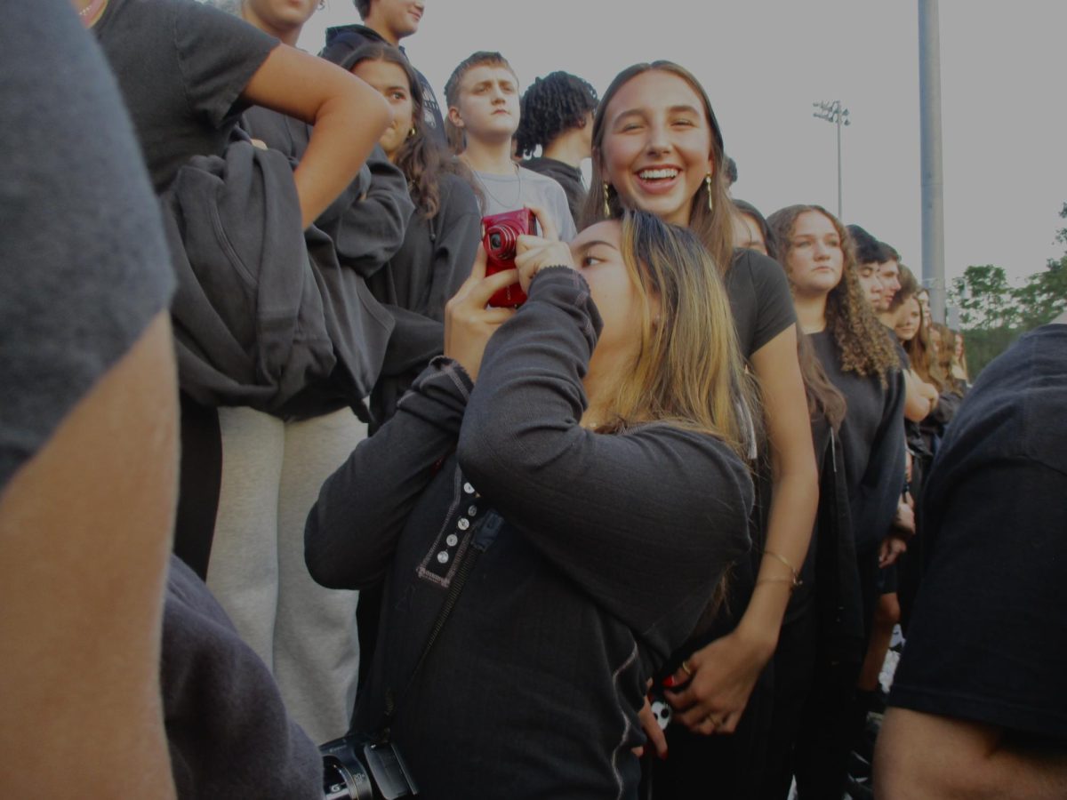 Sophomore Alexys Valda taking a photo with her digital camera at a football game 